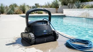 Robotic pool cleaner on the deck beside a clear inground pool
